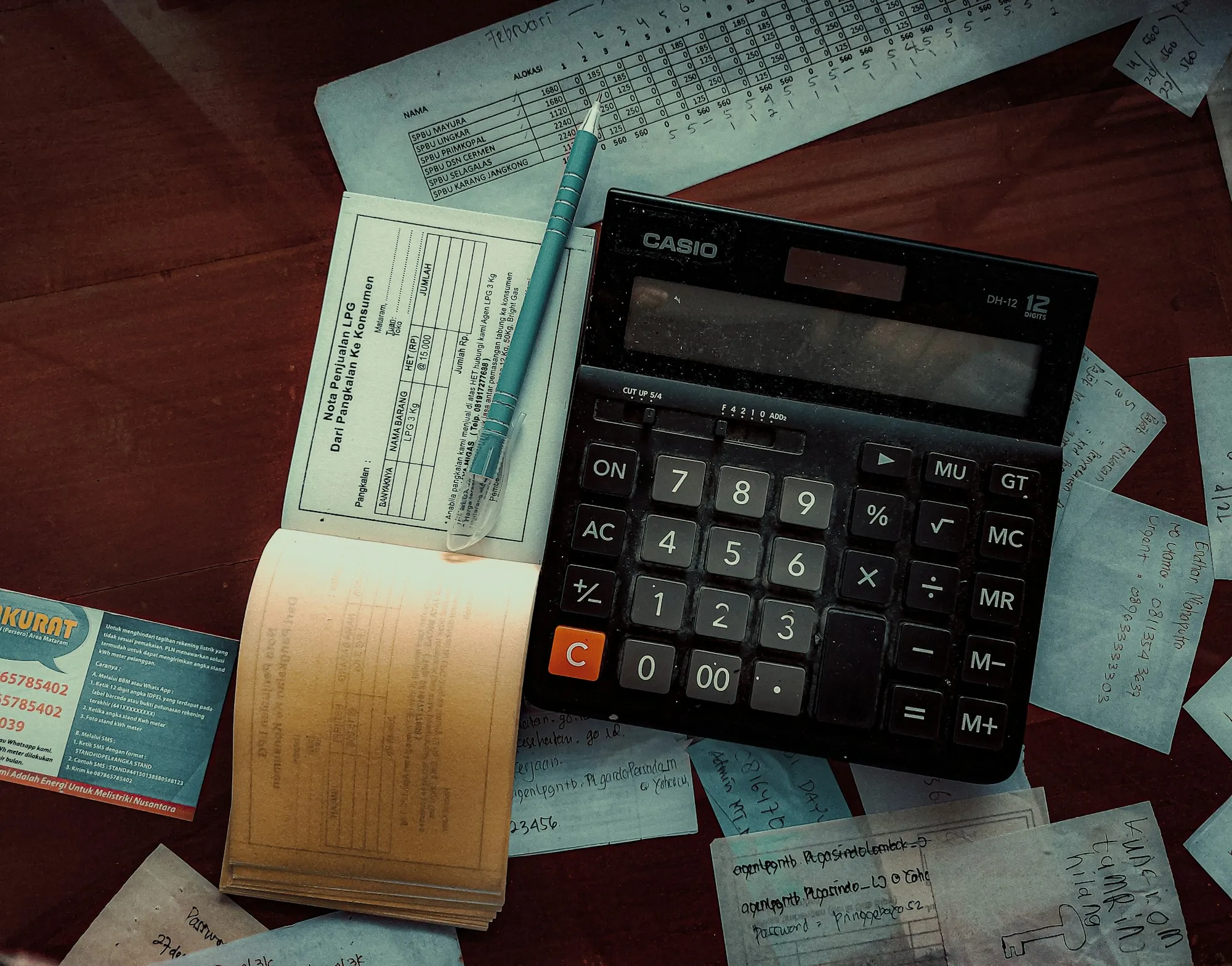 Calculadora sobre uma mesa de madeira, entre recibos e um talão de notas